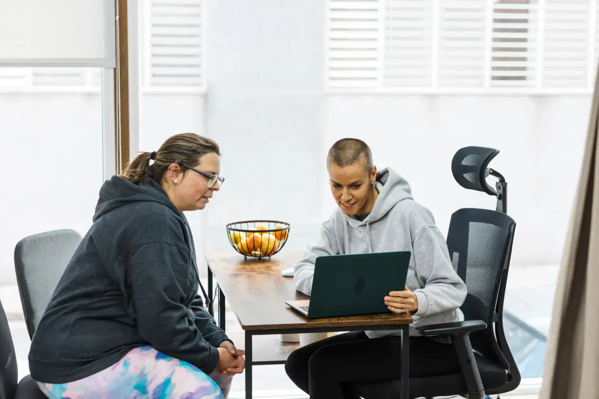 Personal trainer showing a workout plan to a client on a laptop, the kind of plan a 3 month package covers
