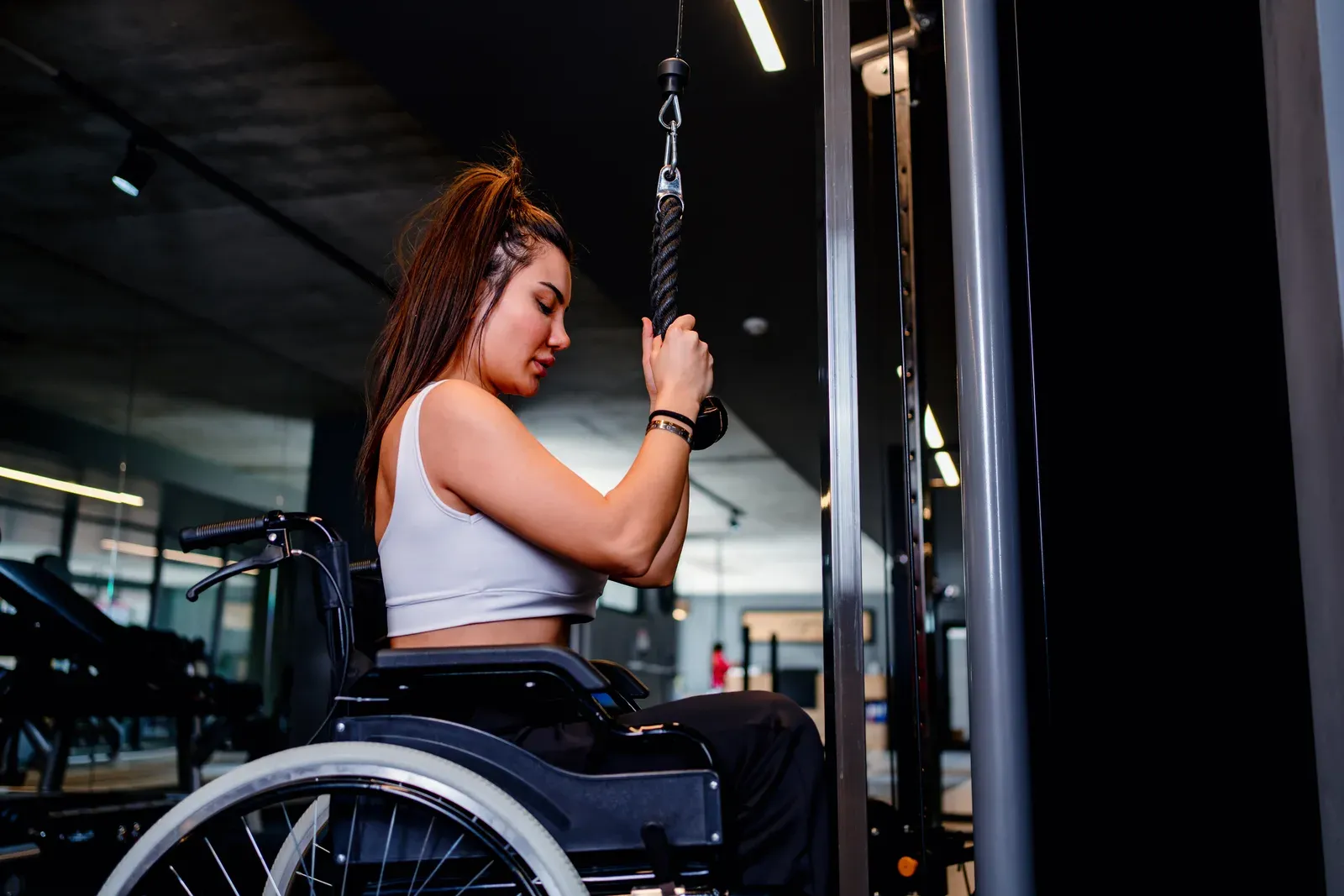 A woman in a wheelchair doing a cable rope pull exercise in a gym
