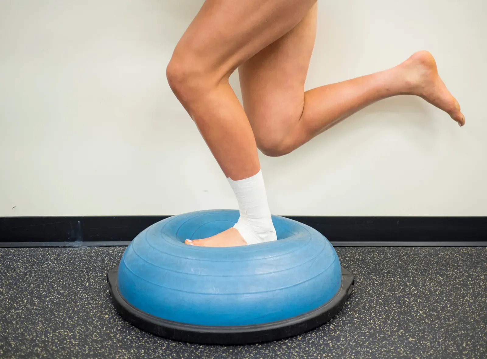 An athlete with a taped ankle balancing on one leg on a balance trainer