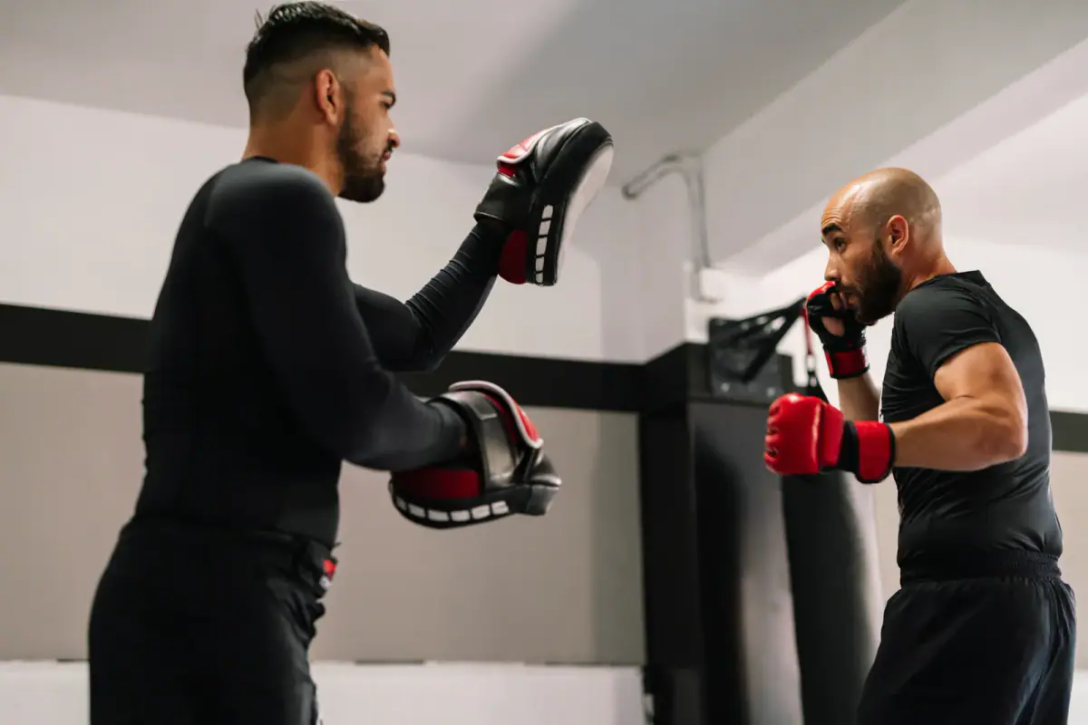 Kickboxer in red boxing gloves kicking toward his trainer's hands during a gym session