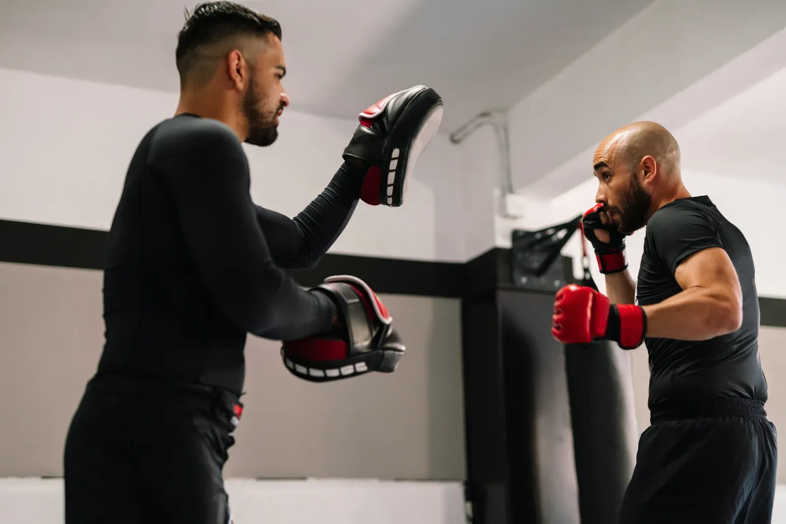 Kickboxer in red boxing gloves kicking toward his trainer's hands during a gym session