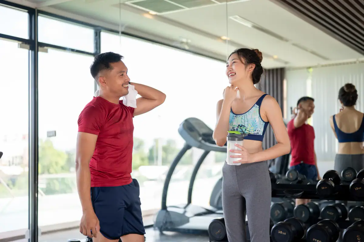 Trainer wiping sweat while a client holds water after exercise, a break that shows why buffer time between clients matters