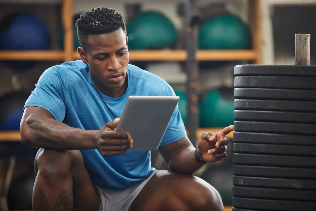Muscular young man using a tablet while checking gym equipment, a trainer covered by a business owners policy