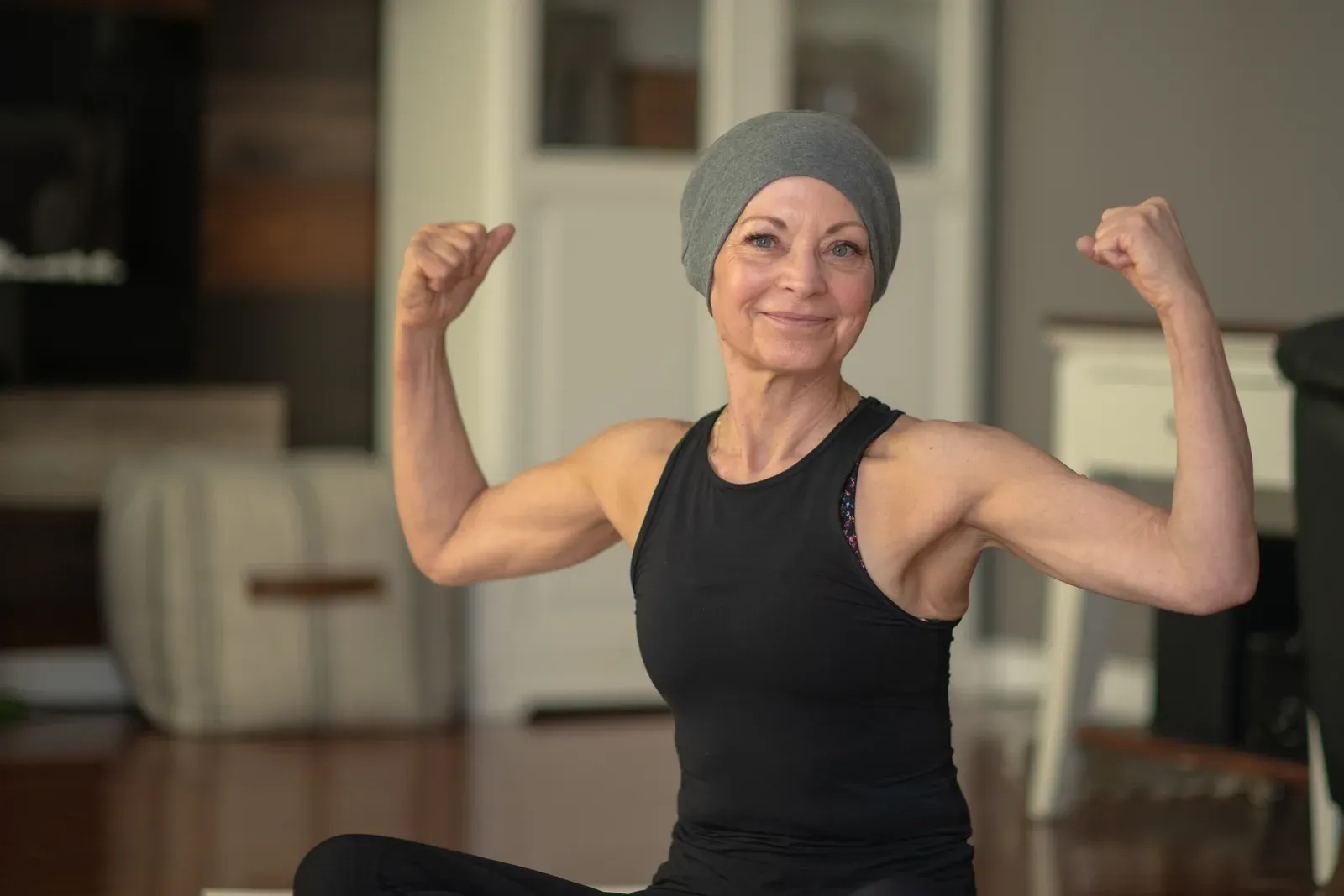 A smiling woman in a head wrap flexing both arms during a workout