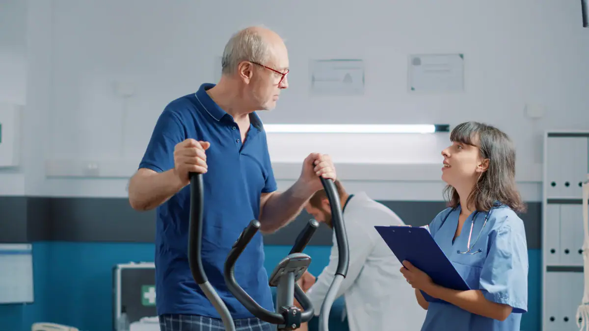 Nurse assisting a patient on a stationary bike, a clinical setting an exercise physiologist may leave for private phase 4 maintenance work