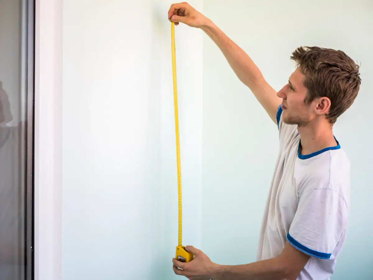 Young man measuring the distance on a wall with a tape measure, a check to make for ceiling height in a training room