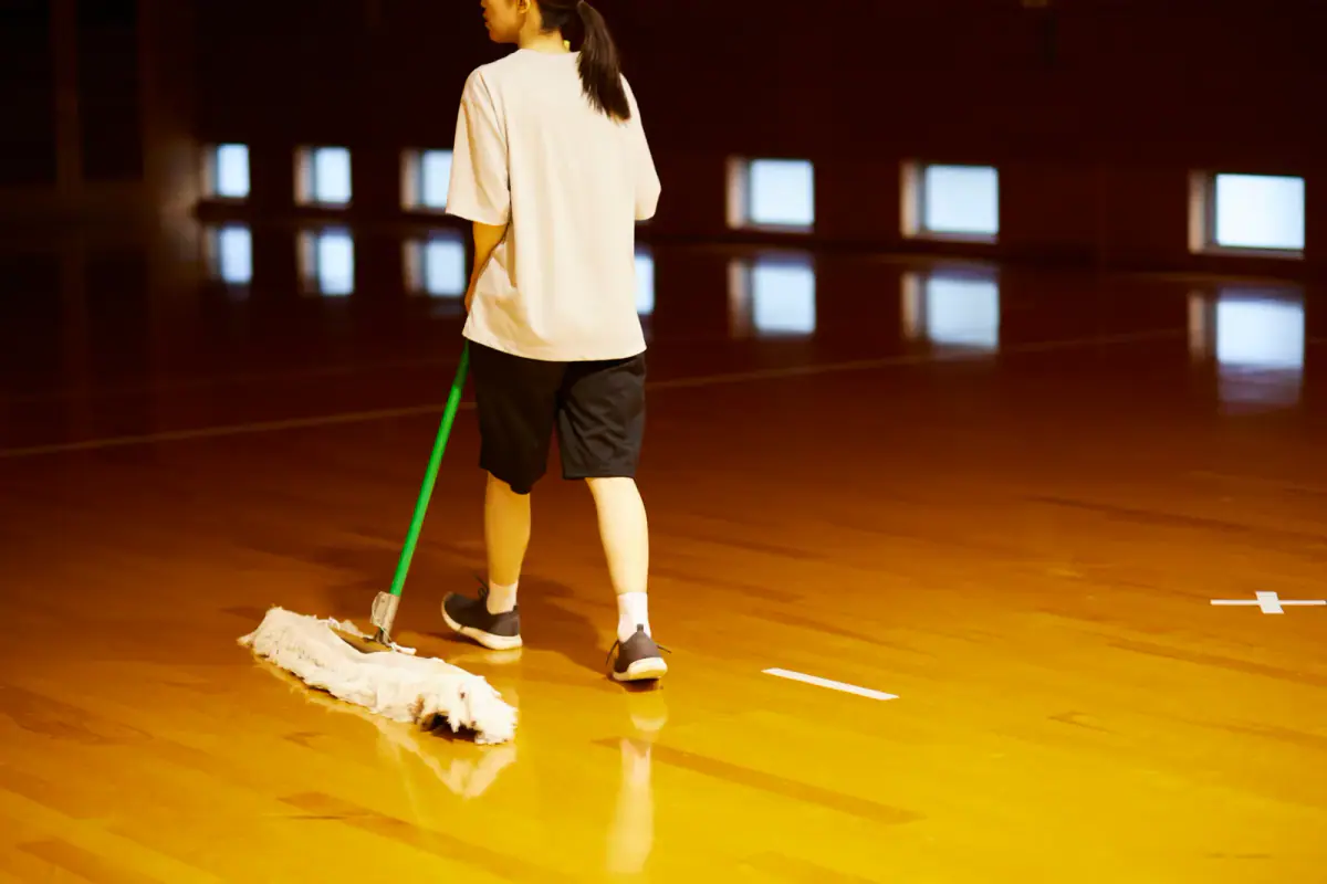Woman cleaning a gymnasium floor with a mop, a task that cleaning fees for rented training space often cover
