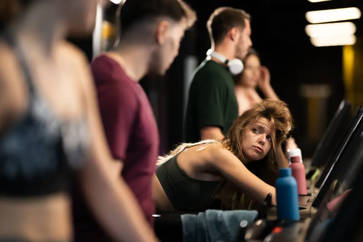 Several people using exercise equipment in a gym during an afternoon session, a busy floor that a private suite avoids