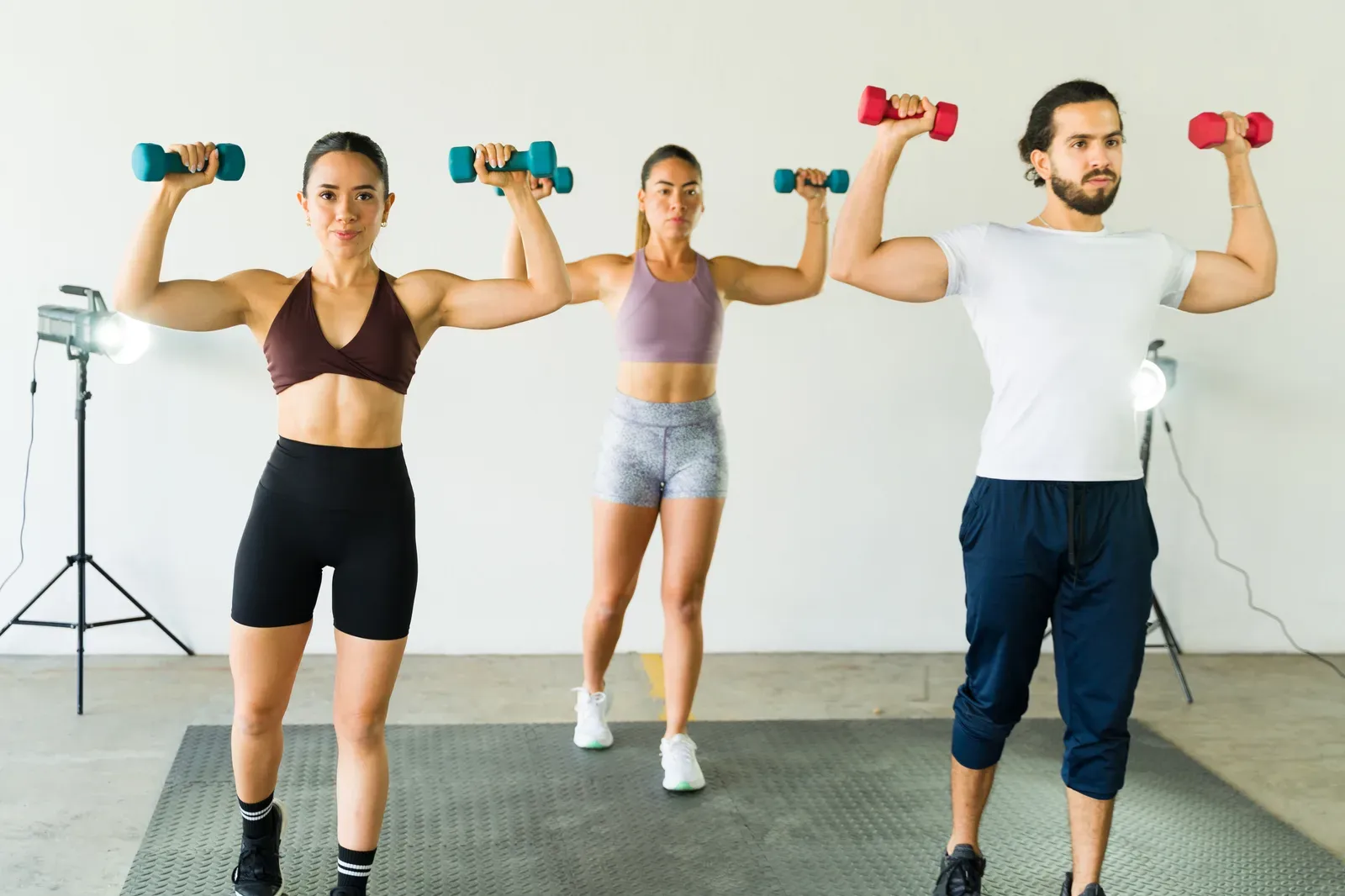 Three people lifting dumbbells together during a small group training session