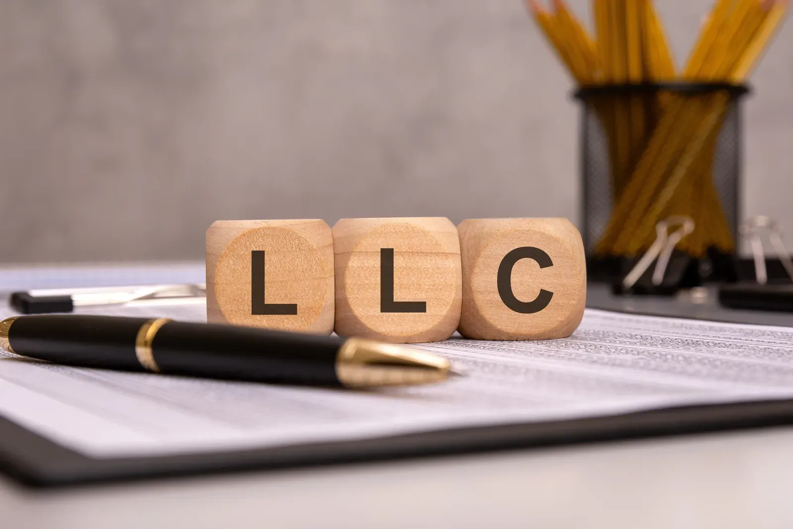 Wooden blocks spelling LLC on a desk beside office documents and a pen