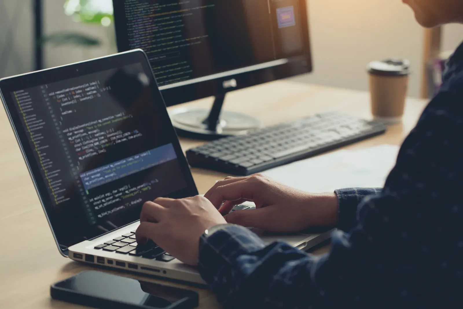 Web designer building a site on a laptop, screens filled with code