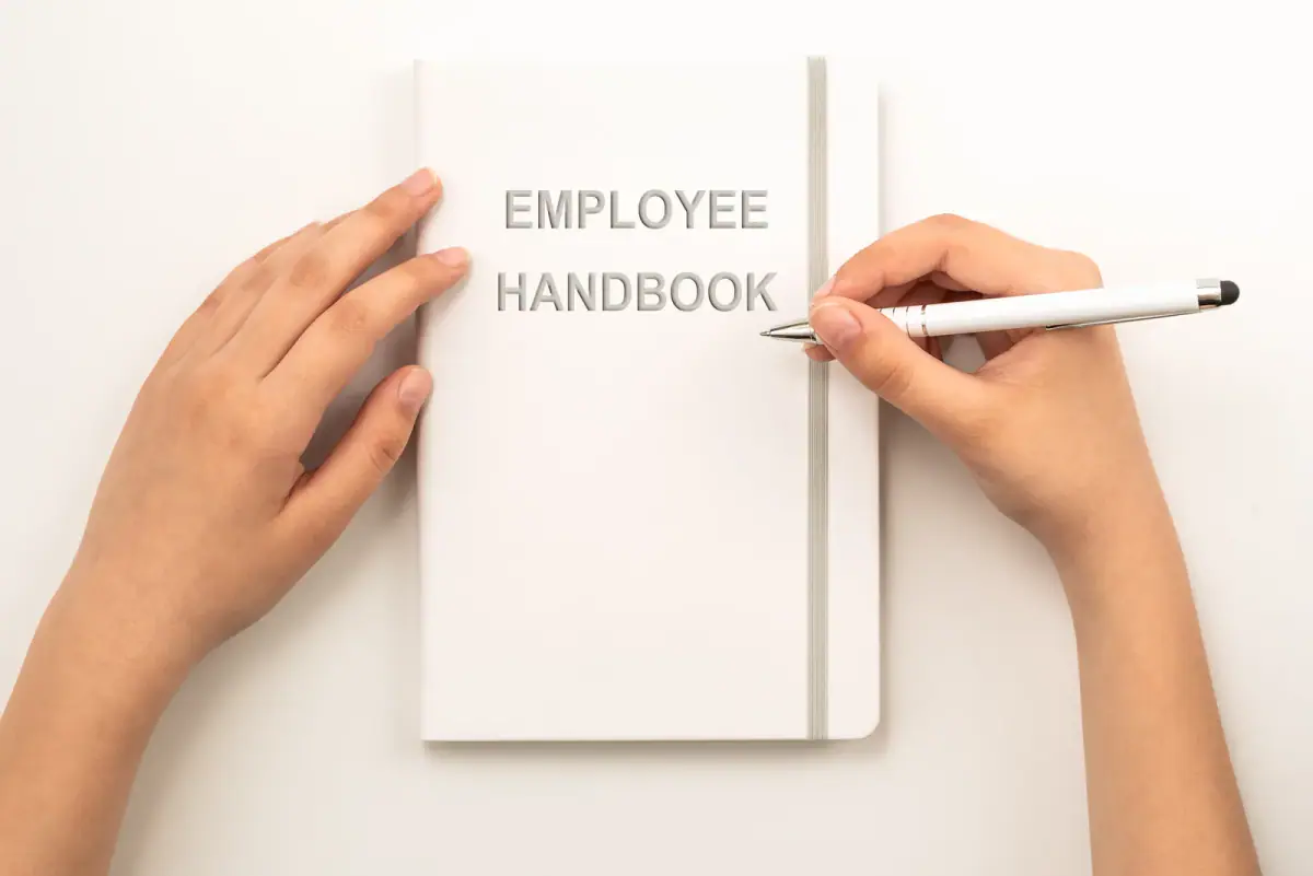 Hands holding a white employee handbook, a document to check when asking if an employer can stop side training work