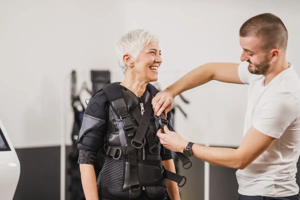 Client exercising in an electro muscle stimulation training suit with a coach adjusting settings
