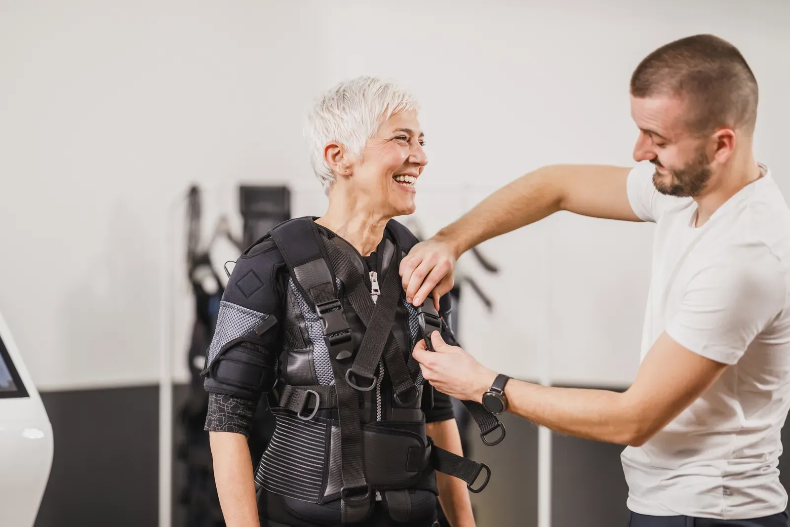 Client exercising in an electro muscle stimulation training suit with a coach adjusting settings