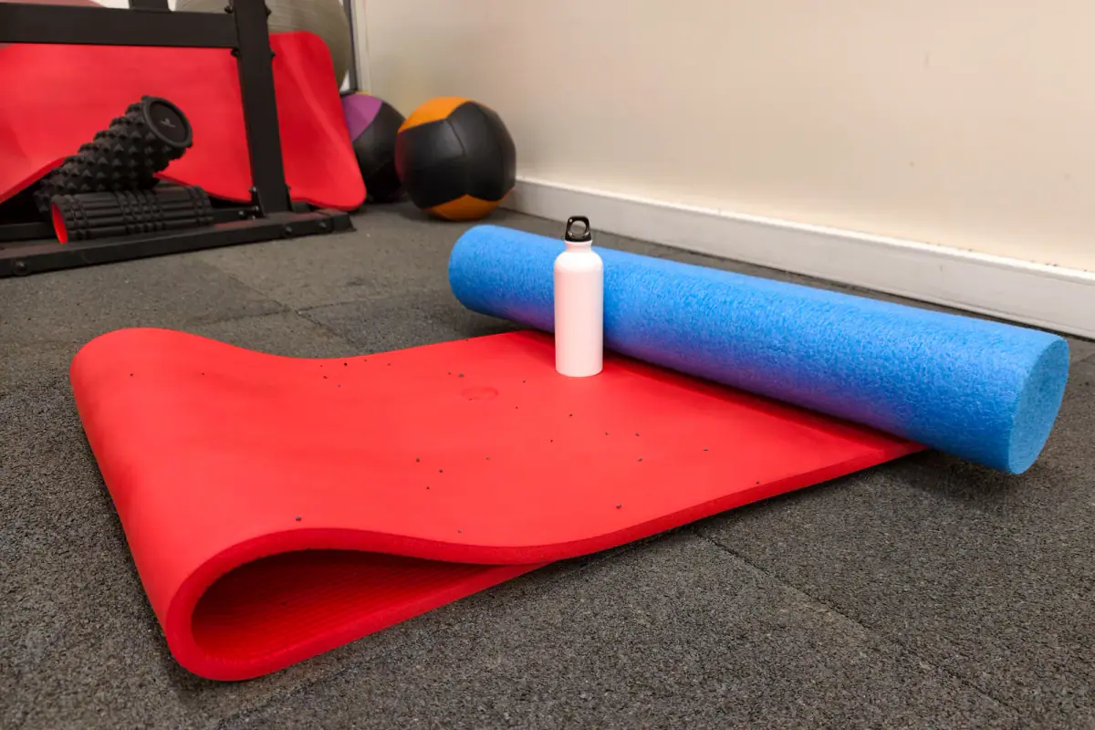 Yoga mat and foam roller with a water bottle on a gym floor, basic gear for a mobility and stretching room equipment list