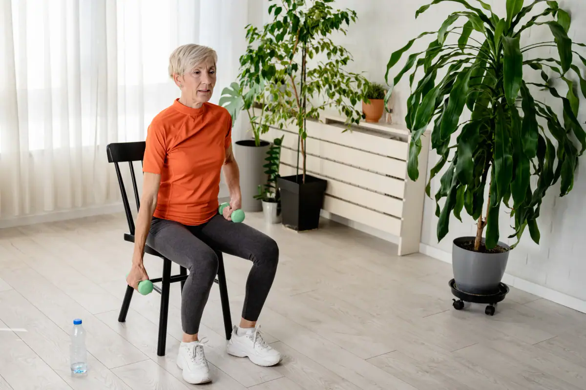 Smiling senior woman instructor doing chair exercises with dumbbells, core gear for a senior fitness session equipment list