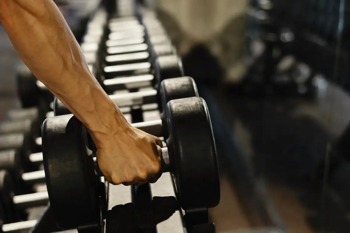Muscular athlete taking a black dumbbell from a rack at the gym, a staple of a strength training room equipment list