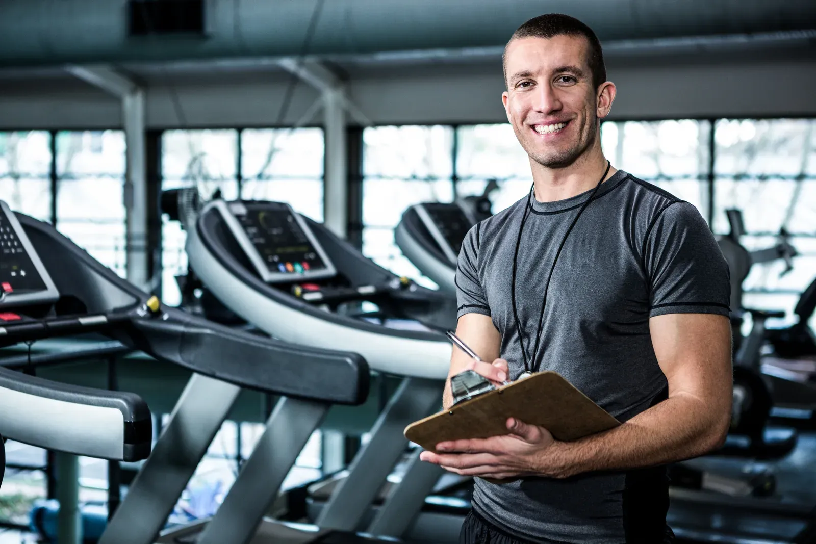 A new personal trainer with a clipboard greeting a client at a gym