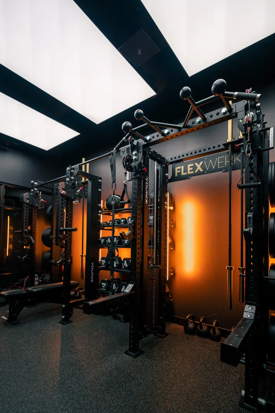 Amber lit private workout room with lifting racks and dumbbells