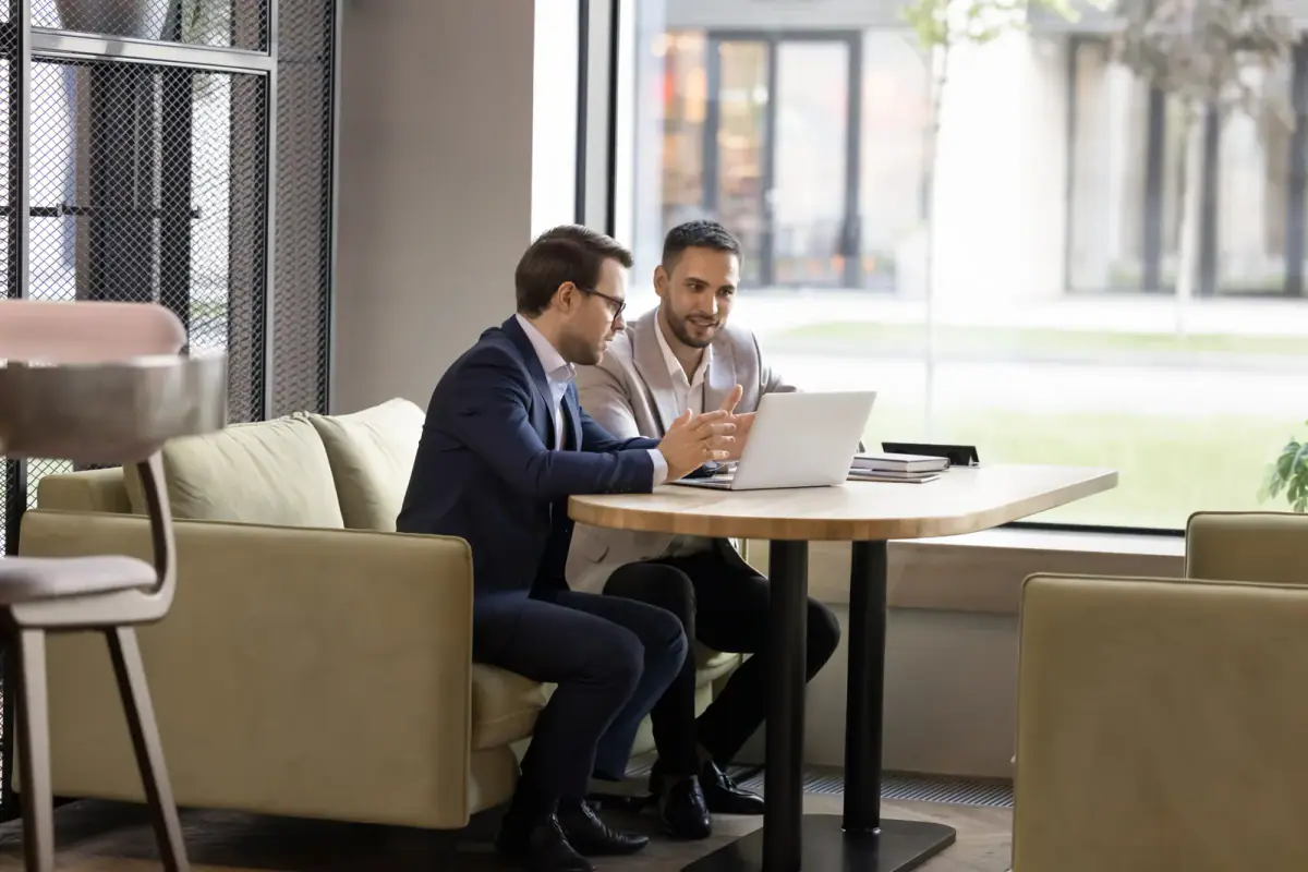 Two business partners talking at a laptop in an office cafe, the start of going into business with another trainer