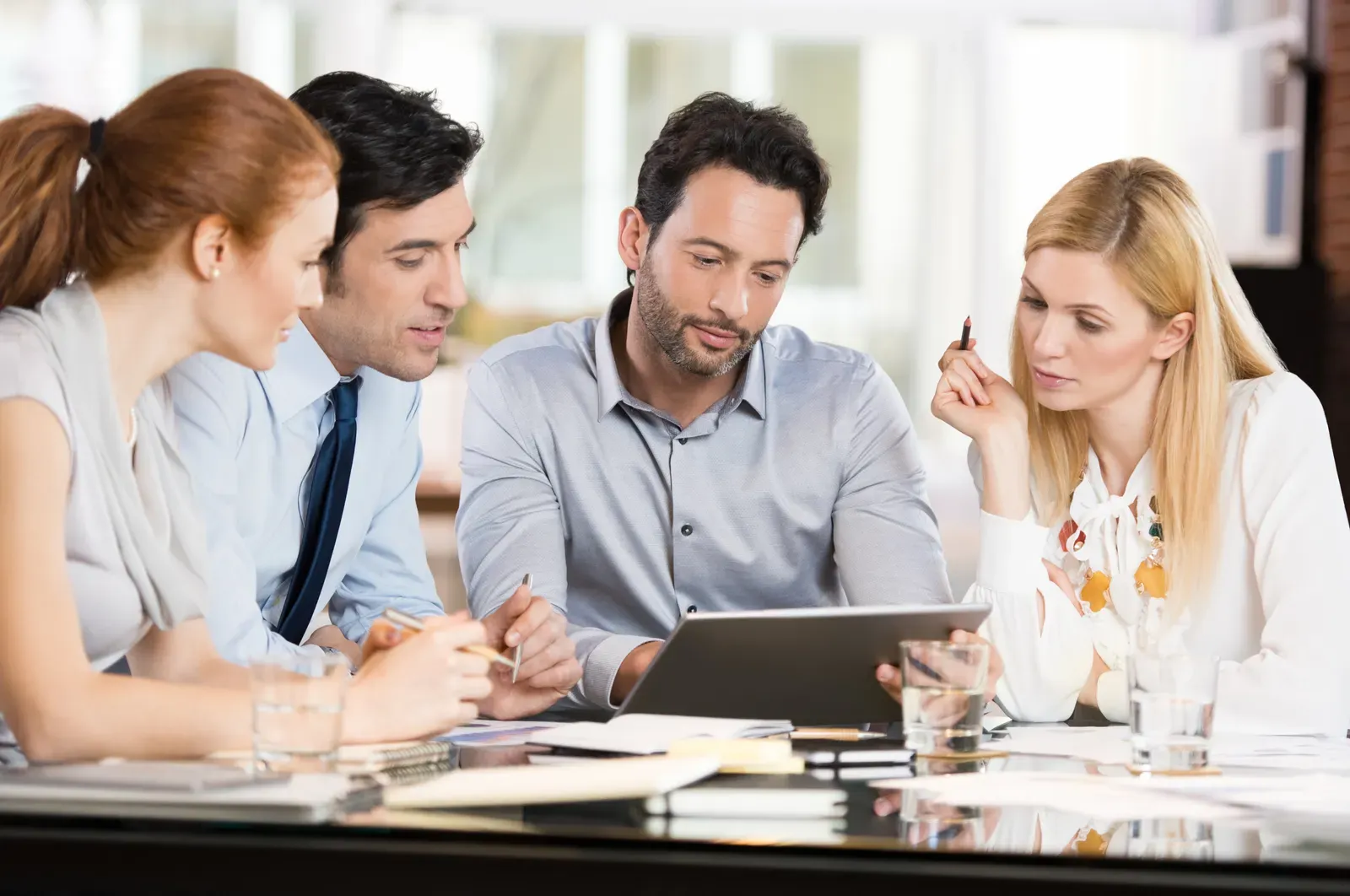 Four colleagues reviewing figures on a tablet at a meeting table