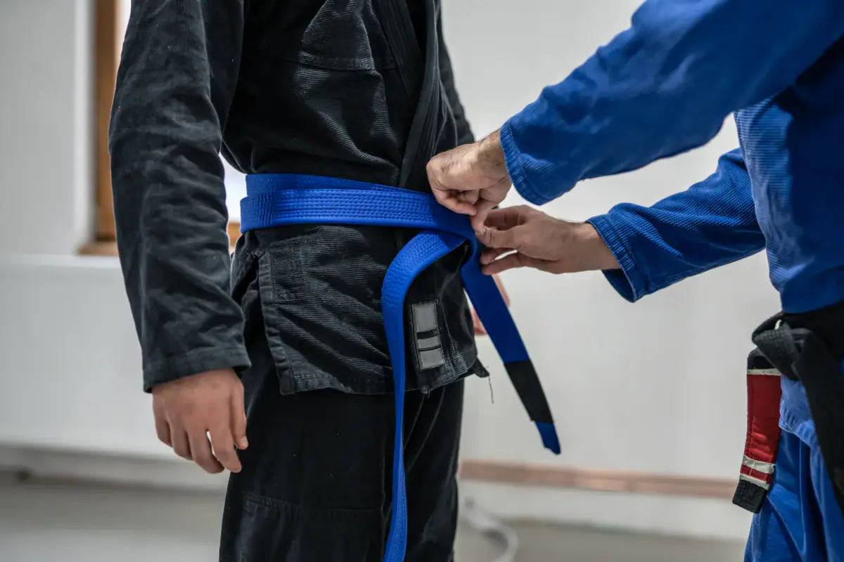 Close up of an instructor hands tying a belt during a jiu jitsu promotion, a belt test that could be held in rented space