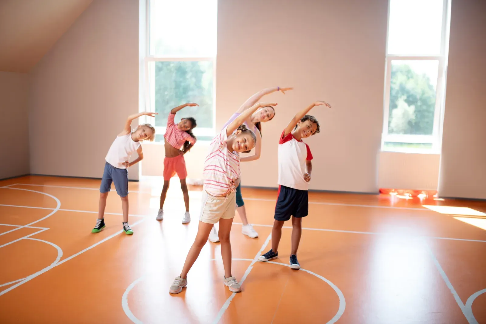 An instructor leading four children through side stretches on an indoor court