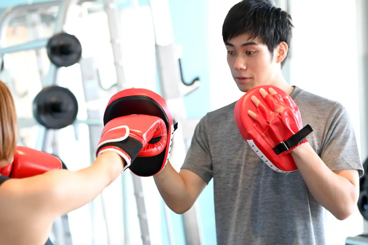 Woman punching at a martial arts gym while a male instructor holds punching mitts, a drill that sets how much room mitt work needs