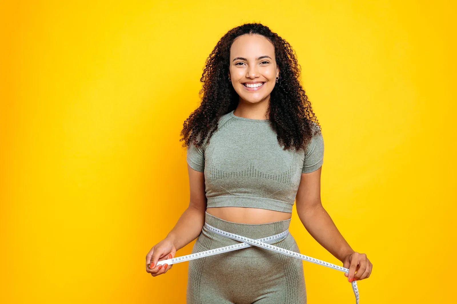 Smiling woman measuring her waist with a tape, tracking progress between reassessments