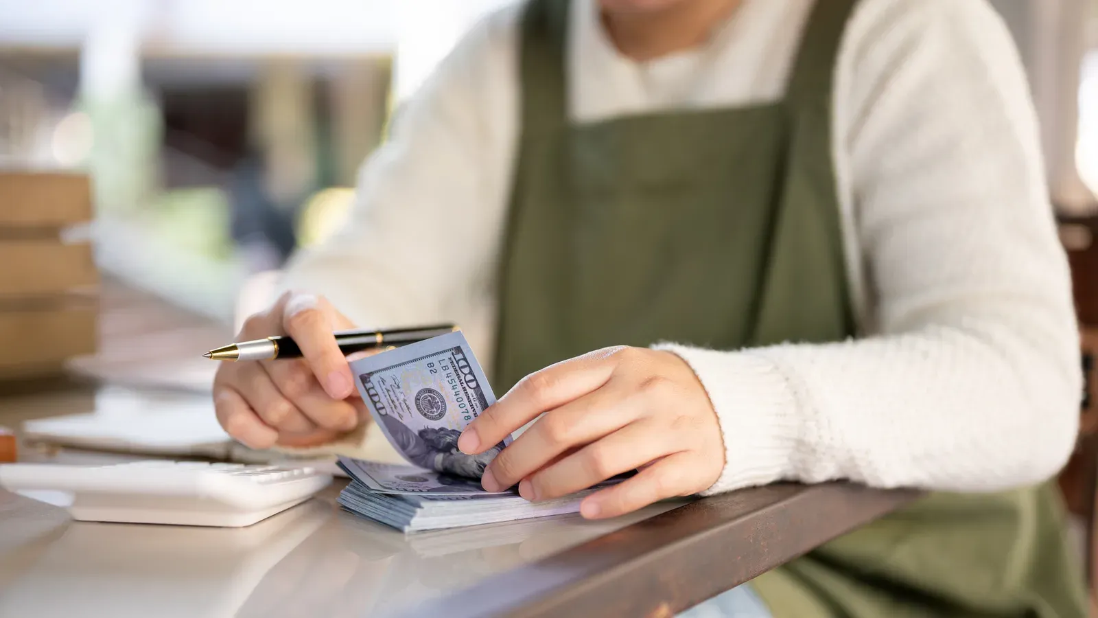 A small business owner working through her budget with a calculator and cash on the counter