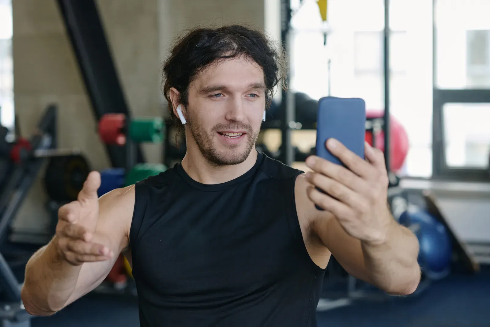 A fitness coach filming a workout video on a phone in the gym