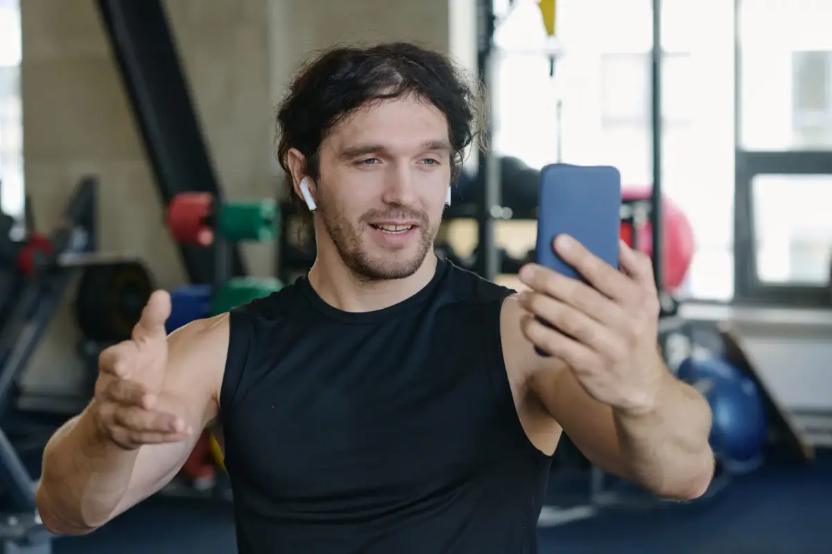 A fitness coach filming a workout video on a phone in the gym
