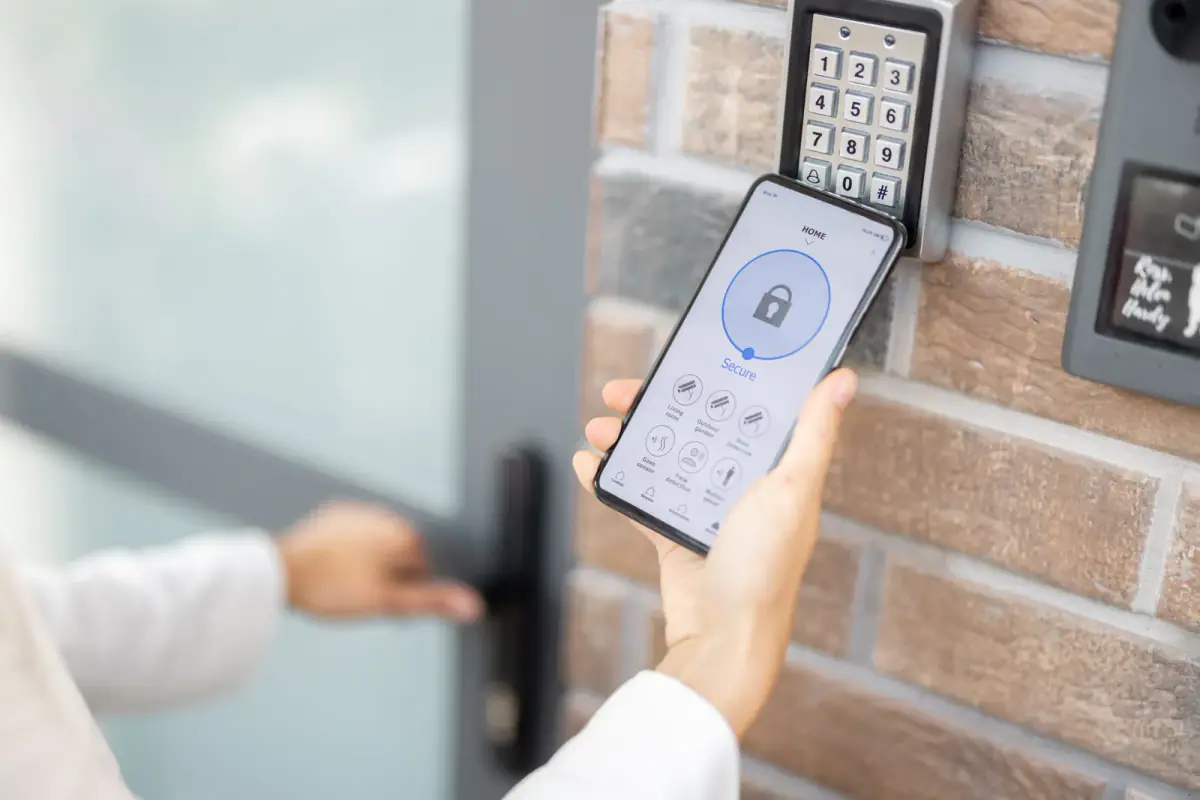 Person unlocking a door with a smartphone next to a wall keypad, a common keyless entry setup for rented rooms