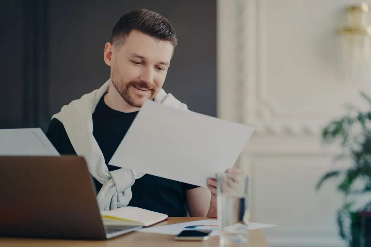Male freelancer concentrating on papers and a financial report at a desktop, a close read of a license vs lease for hourly space
