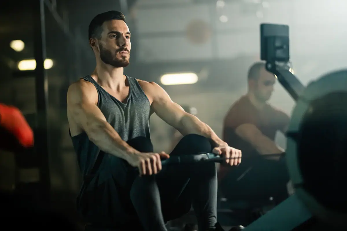 Young athletic man doing cross training on a rowing machine in a health club, a way to fit lifting and cardio in one hour