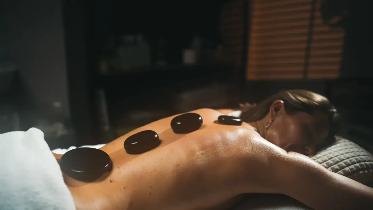 Relaxed woman receiving a hot stone massage, a service that needs oils and stones planned for in a rented suite