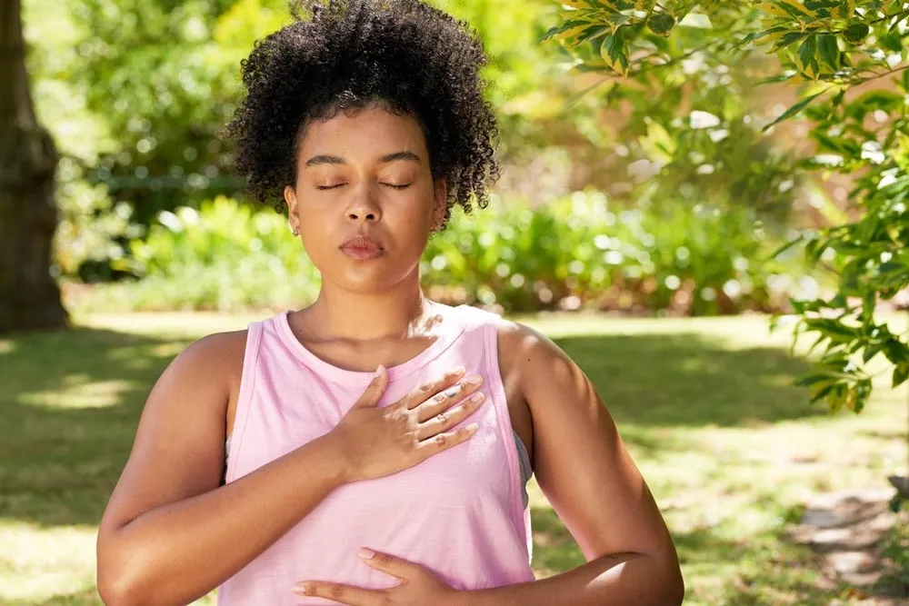 A woman with closed eyes practicing a breathing exercise with a hand on her chest
