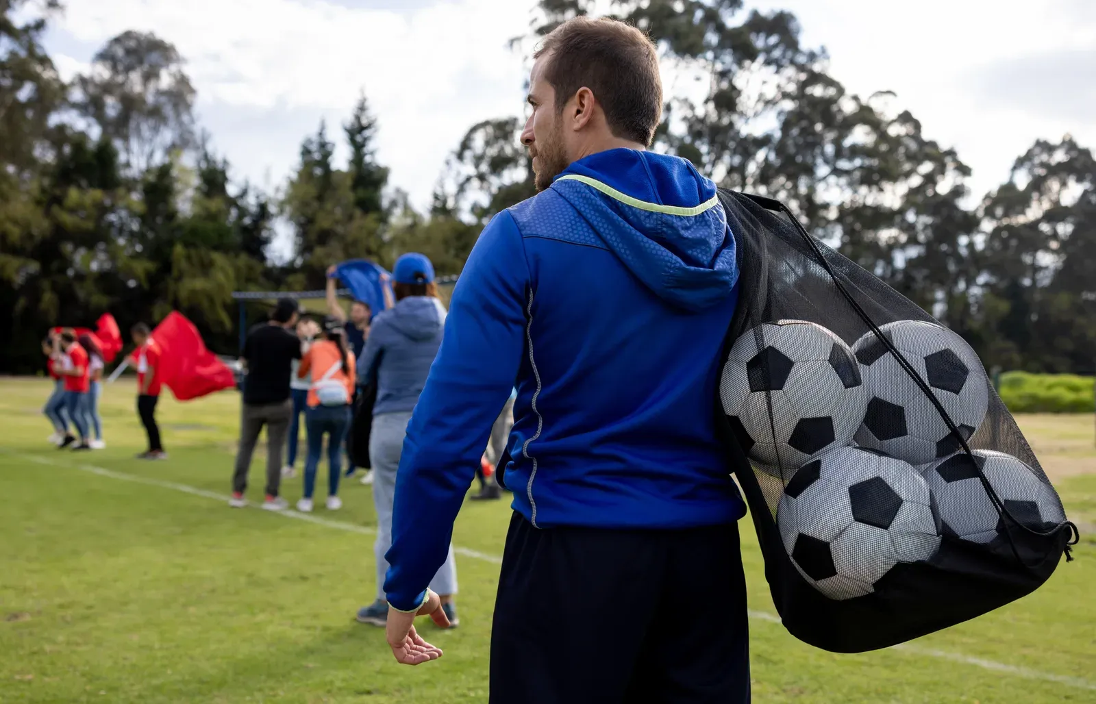 Coach carrying a mesh bag of soccer balls at the end of practice