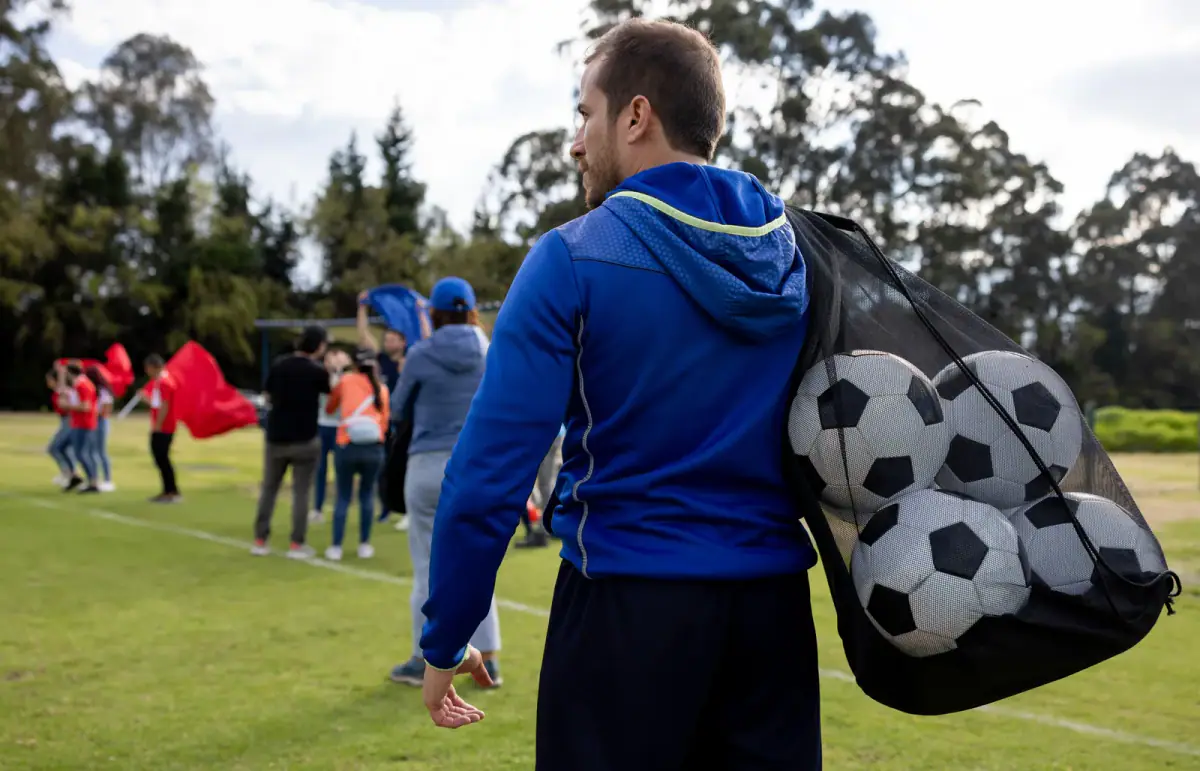 Coach carrying a mesh bag of soccer balls at the end of practice