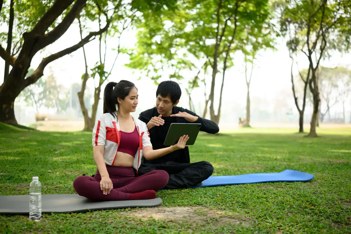 A personal trainer and client reviewing a workout plan on a tablet during an outdoor session, as in mobile training