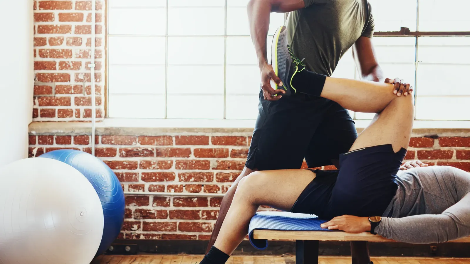 A coach guiding a client through a deep hip stretch on the floor