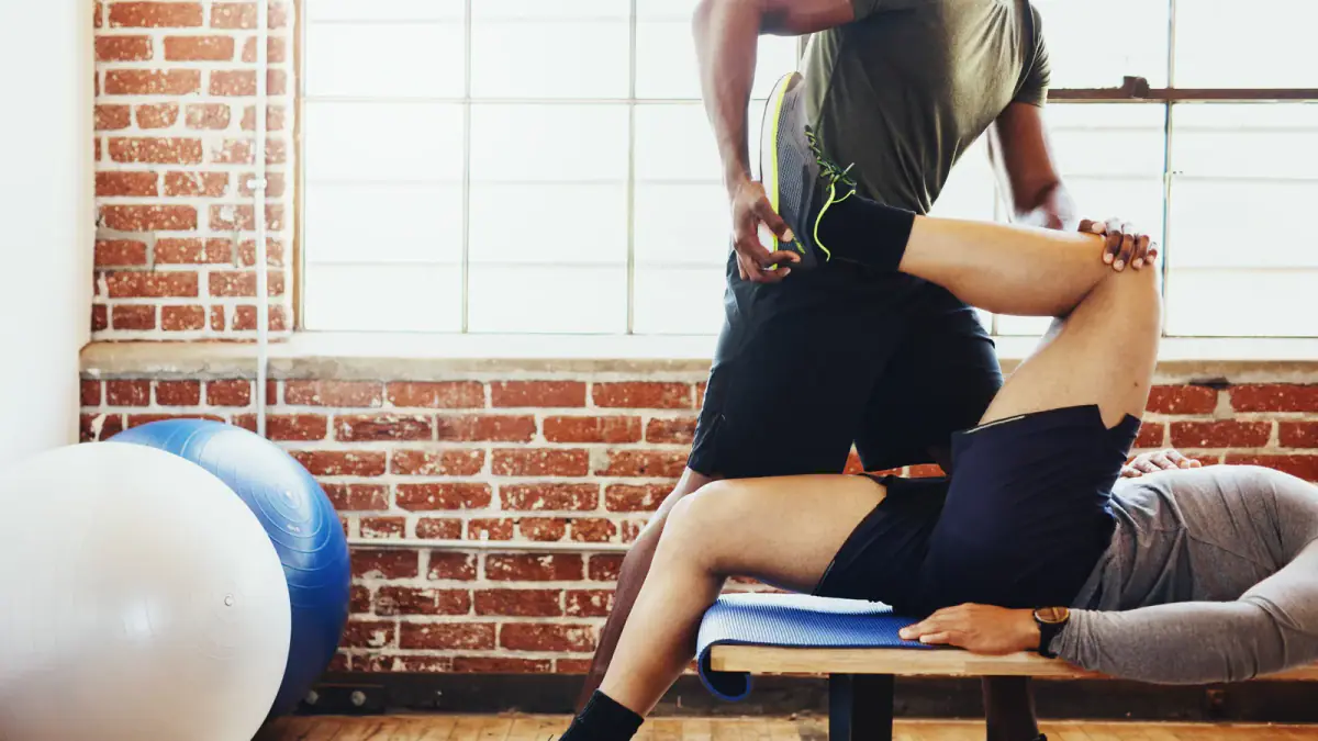 A coach guiding a client through a deep hip stretch on the floor