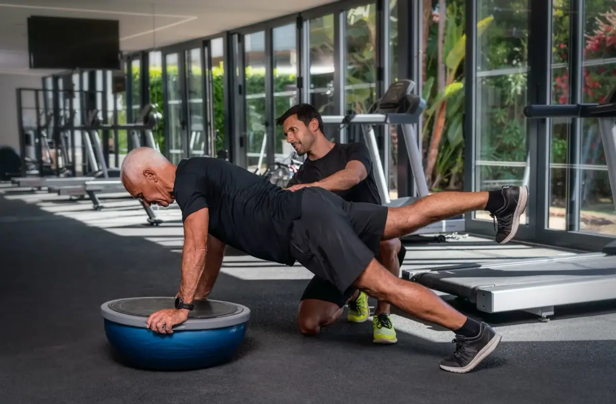 Older adult practicing balance work while a trainer stands close with a steadying hand