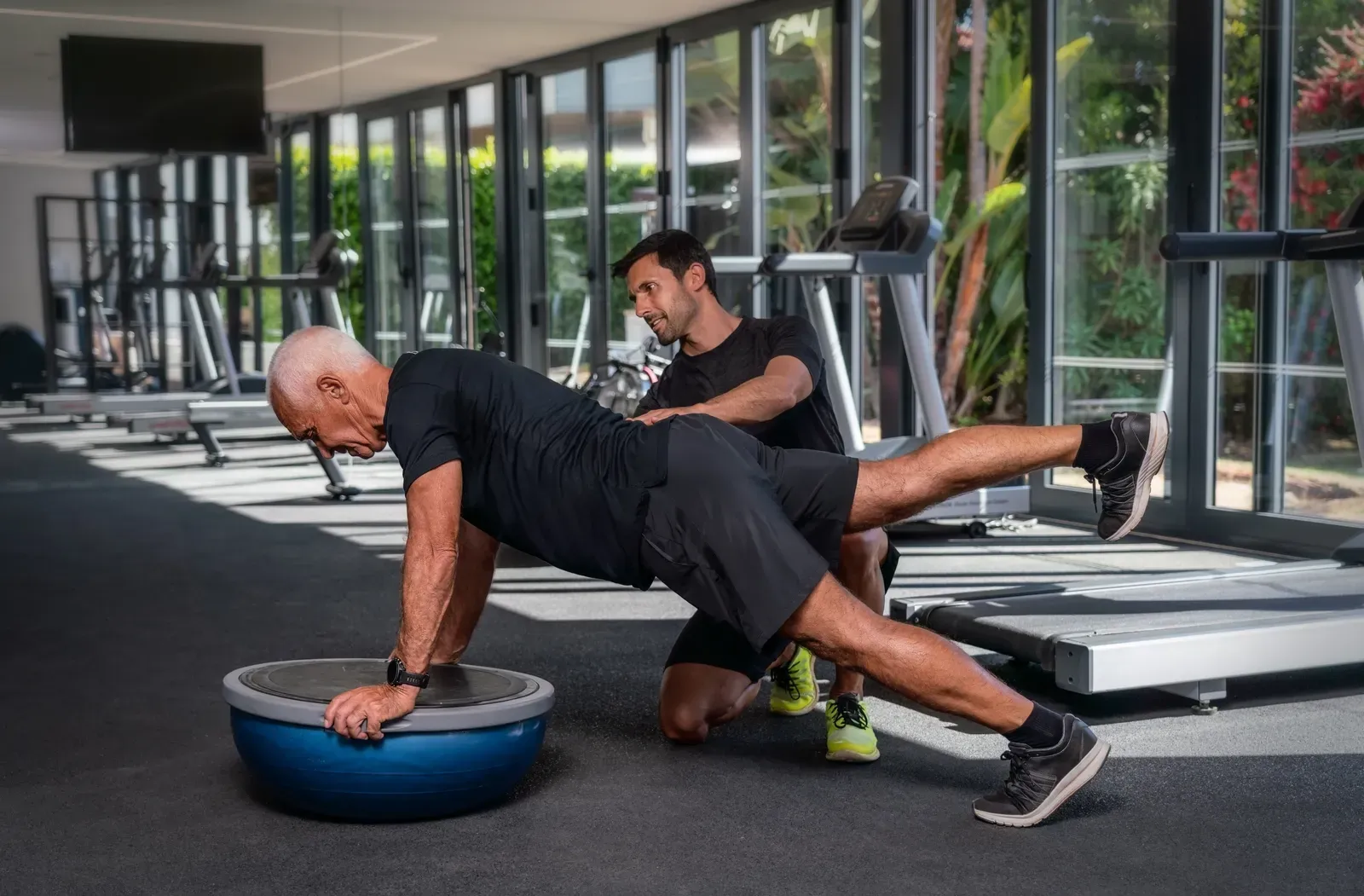 Older adult practicing balance work while a trainer stands close with a steadying hand