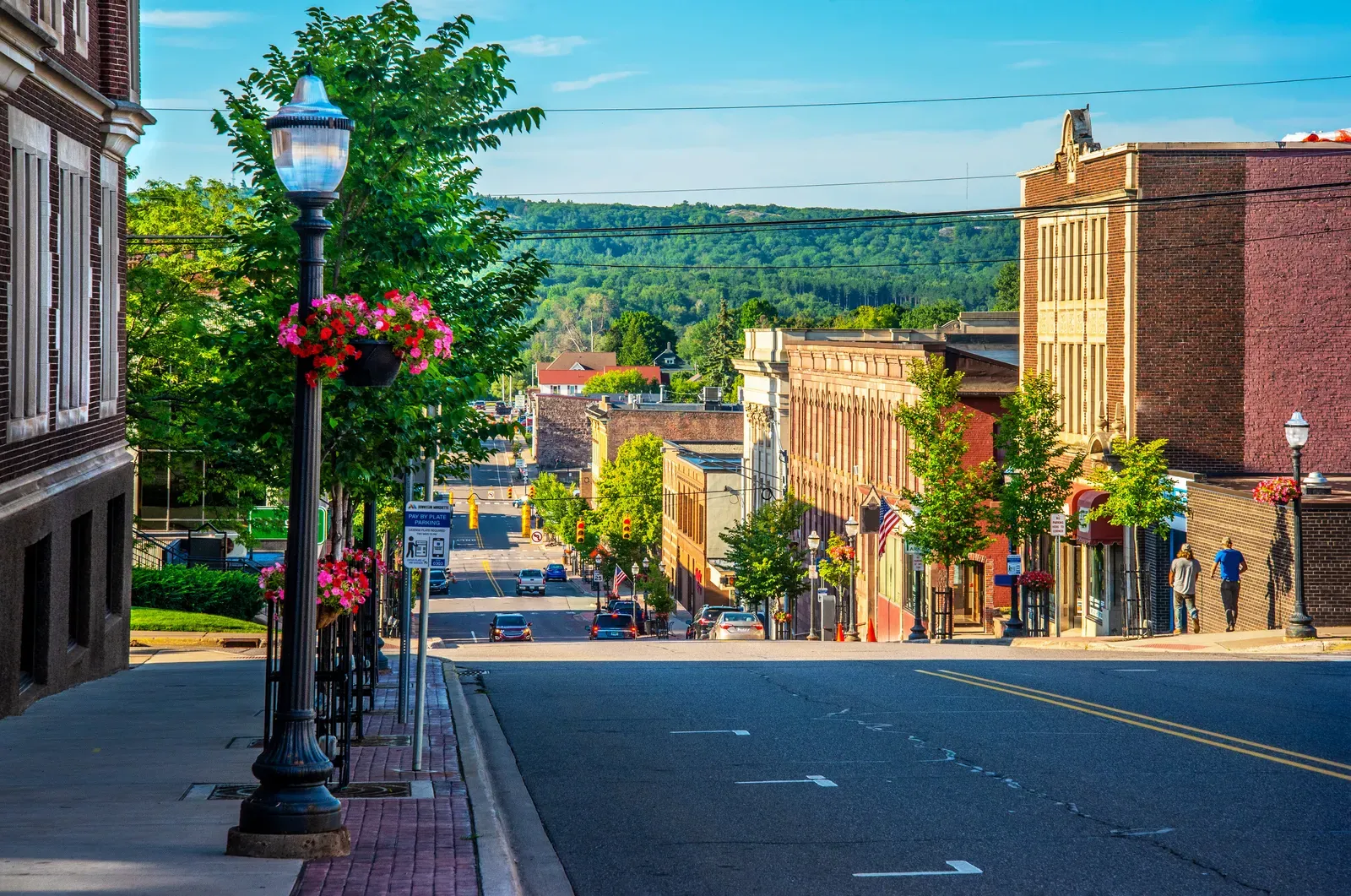 Historic small city main street with lampposts, storefronts, and wooded hills beyond