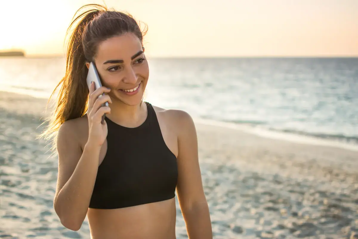 Smiling young woman talking on her mobile phone at the beach, a vacation that clients should hear about with proper notice