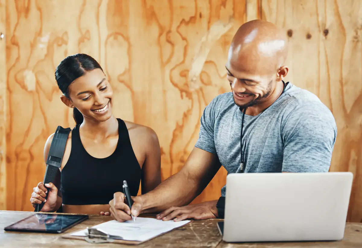 Young man filling out paperwork while assisting a client in a gym, a setup for offering a payment plan on an expensive training package