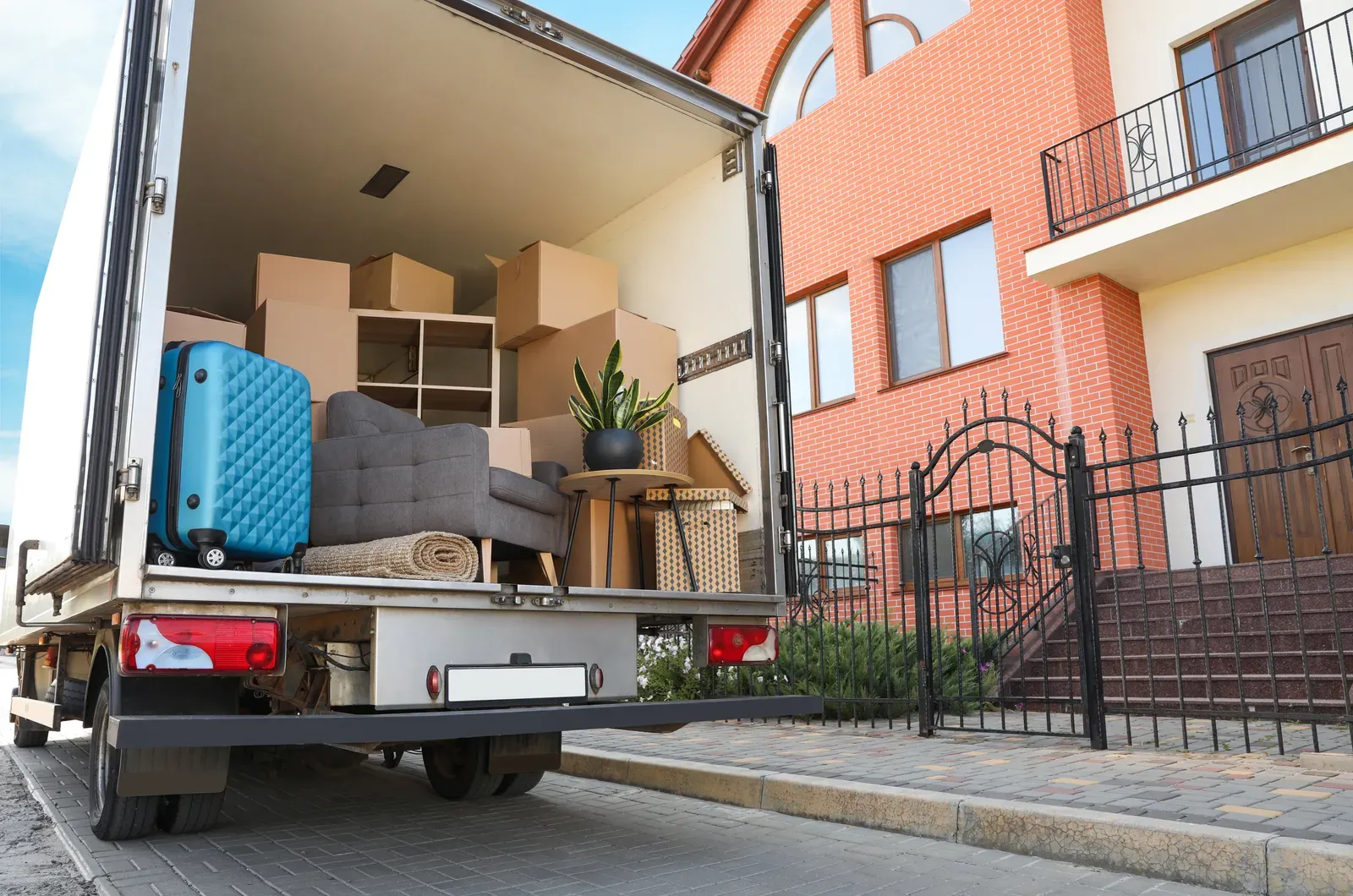 Open moving truck packed with boxes and furniture outside a brick house