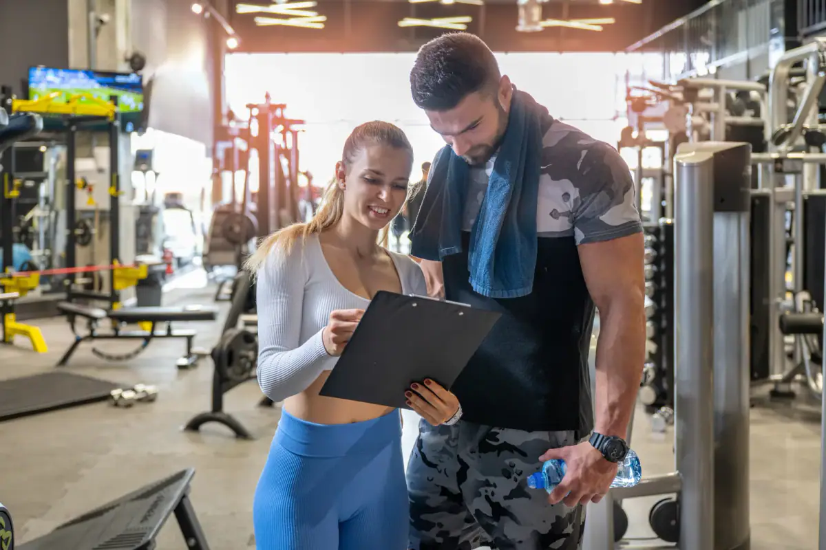 A young female personal trainer discussing a male client's workout progress at the gym, like a progress report