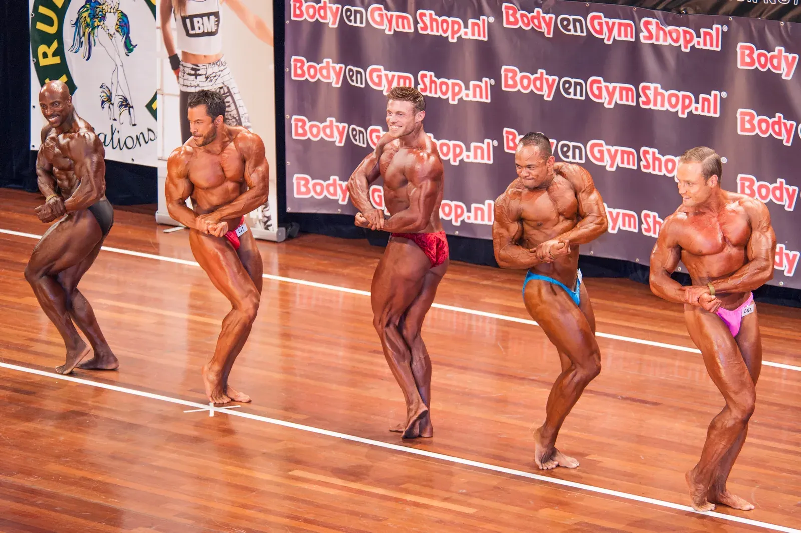 Male bodybuilders hitting poses in a lineup on a competition stage